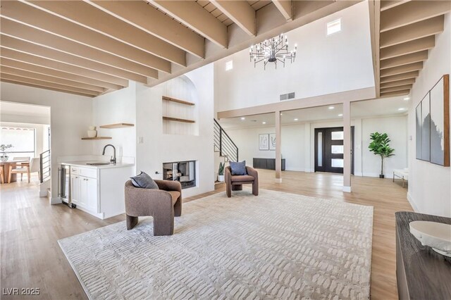 living room featuring light wood finished floors, visible vents, beamed ceiling, and a multi sided fireplace