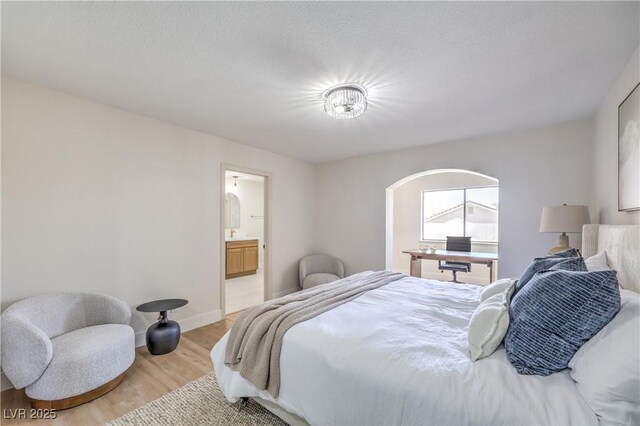 bedroom featuring a textured ceiling, light wood-type flooring, connected bathroom, and baseboards