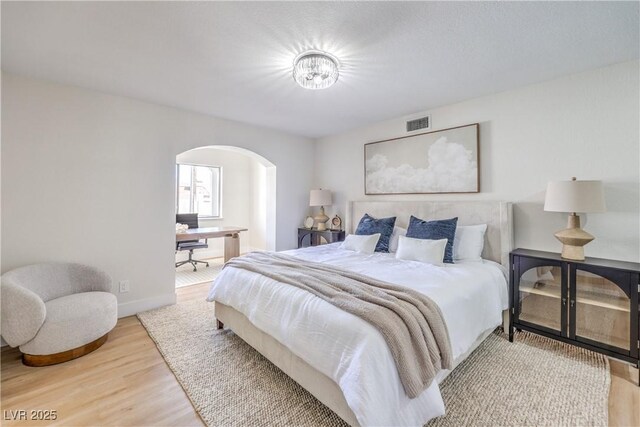 bedroom with baseboards, visible vents, arched walkways, and wood finished floors