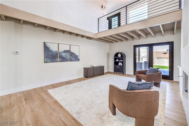 living area with beam ceiling, a high ceiling, light wood-style flooring, and baseboards