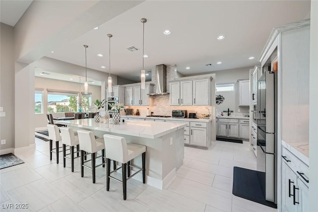 kitchen with appliances with stainless steel finishes, a breakfast bar, hanging light fixtures, wall chimney exhaust hood, and a spacious island