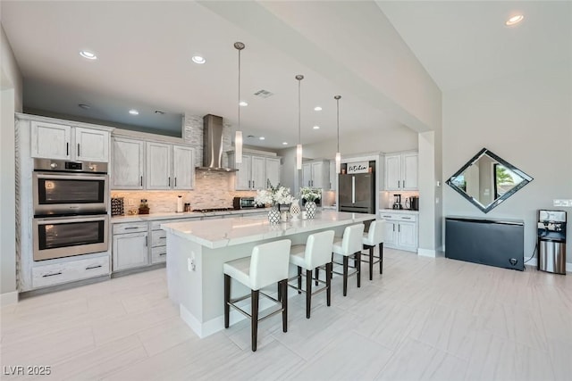 kitchen with pendant lighting, stainless steel appliances, a kitchen breakfast bar, a spacious island, and wall chimney exhaust hood