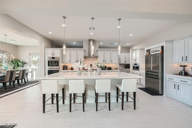 kitchen with a spacious island, white cabinetry, hanging light fixtures, stainless steel appliances, and wall chimney range hood