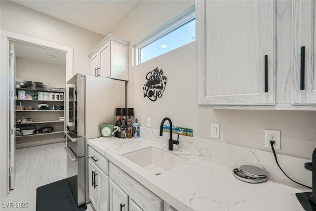 kitchen with white cabinetry, light stone countertops, sink, and stainless steel refrigerator