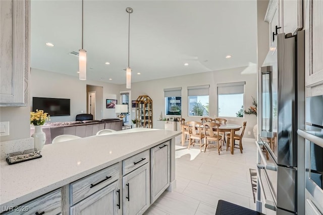 kitchen with stainless steel fridge, light stone countertops, and hanging light fixtures