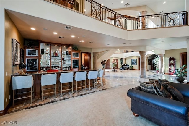 bar featuring decorative columns, carpet, and a high ceiling