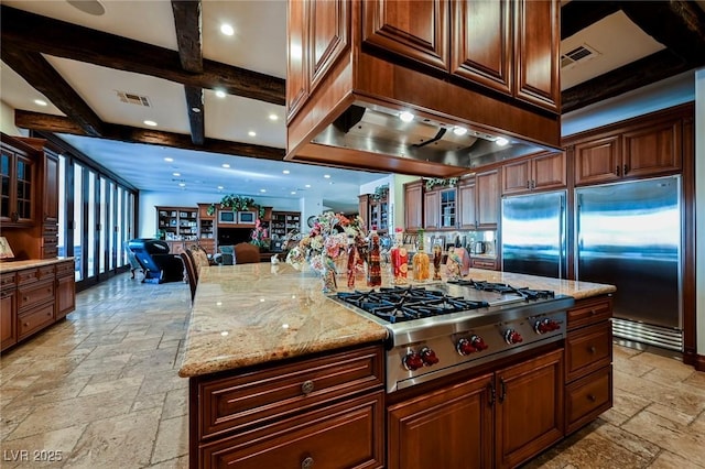 kitchen with stainless steel appliances, a kitchen island, light stone counters, and beam ceiling