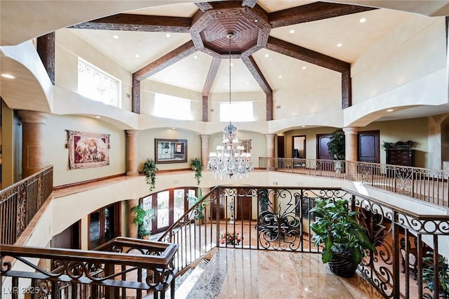 interior space with an inviting chandelier, a towering ceiling, beam ceiling, and ornate columns