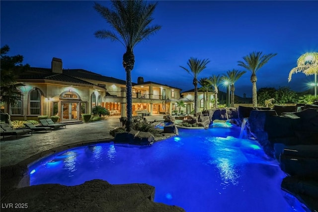 pool at night featuring a patio area and pool water feature