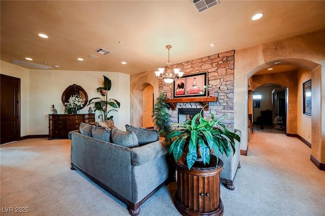 carpeted living room with a stone fireplace and a chandelier