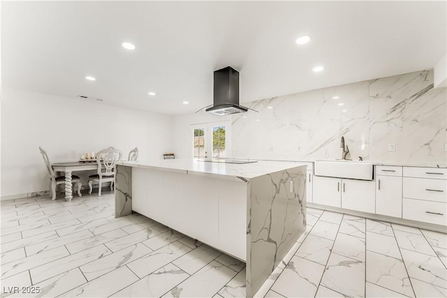 kitchen featuring a large island, sink, white cabinetry, light stone counters, and island exhaust hood