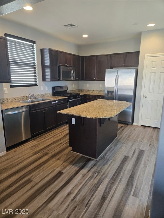 kitchen with visible vents, a kitchen island, appliances with stainless steel finishes, dark wood-type flooring, and a sink