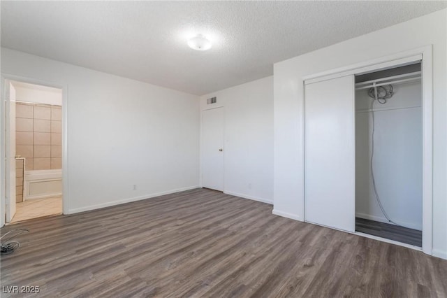 unfurnished bedroom featuring dark hardwood / wood-style flooring, connected bathroom, a closet, and a textured ceiling