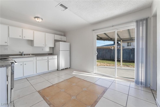 kitchen with white refrigerator, sink, light tile patterned floors, and white cabinets