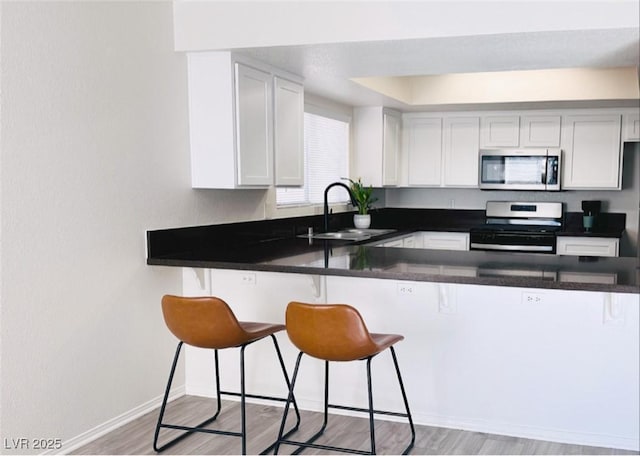 kitchen with a kitchen bar, sink, white cabinetry, kitchen peninsula, and stainless steel appliances