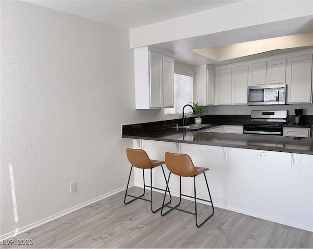 kitchen with appliances with stainless steel finishes, sink, white cabinets, a kitchen breakfast bar, and kitchen peninsula