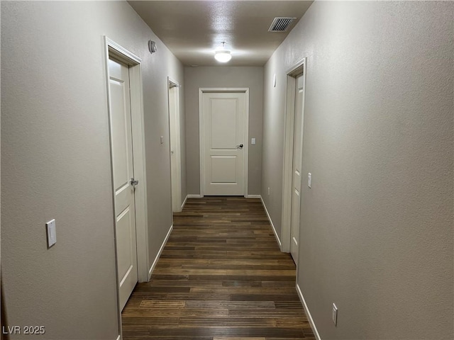 hall featuring dark wood-style floors, baseboards, and visible vents