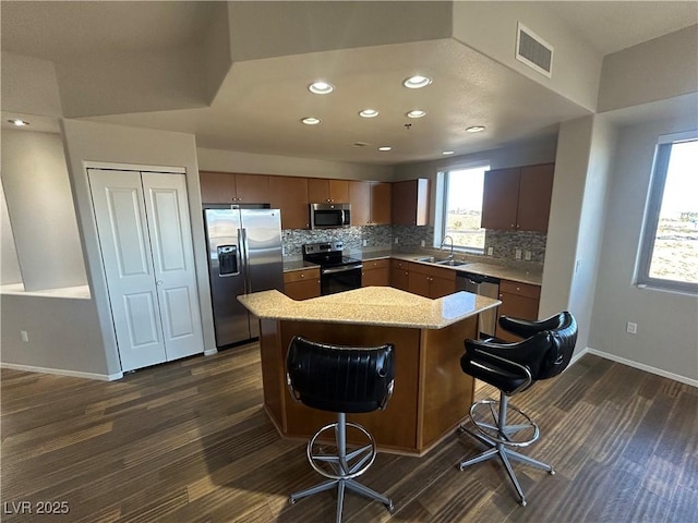 kitchen featuring a breakfast bar area, stainless steel appliances, a sink, visible vents, and decorative backsplash