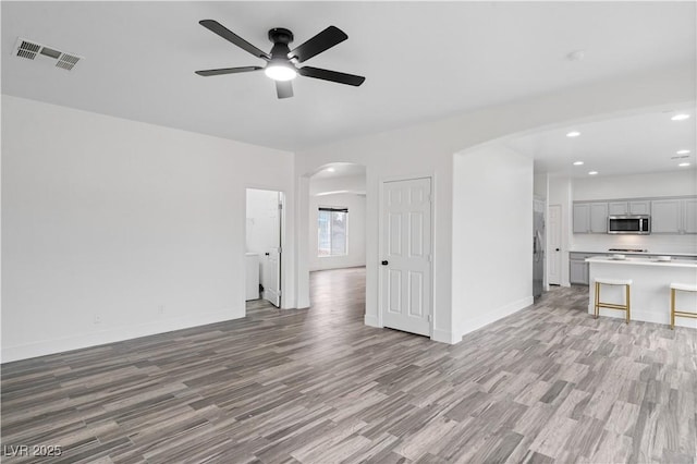 unfurnished living room with arched walkways, visible vents, light wood-style floors, a ceiling fan, and baseboards