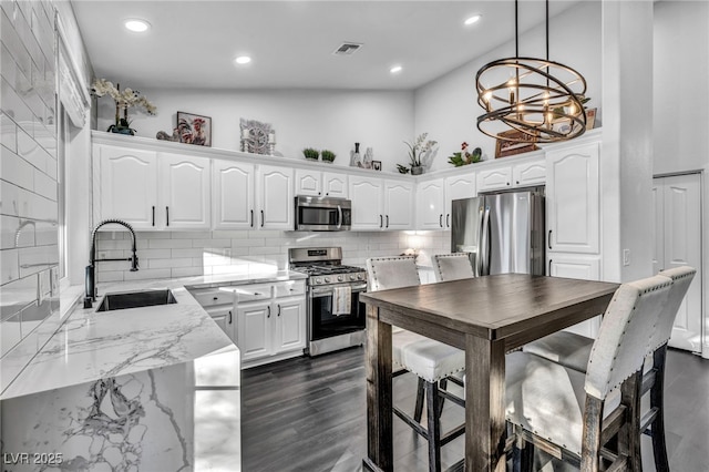 kitchen featuring sink, white cabinets, backsplash, hanging light fixtures, and stainless steel appliances