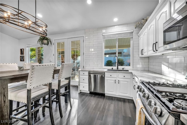 kitchen with white cabinetry, appliances with stainless steel finishes, light stone counters, and decorative light fixtures