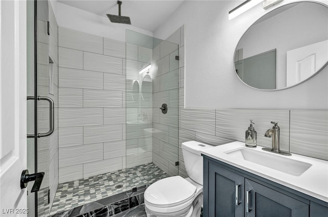 bathroom featuring vanity, toilet, a shower with shower door, and tile walls