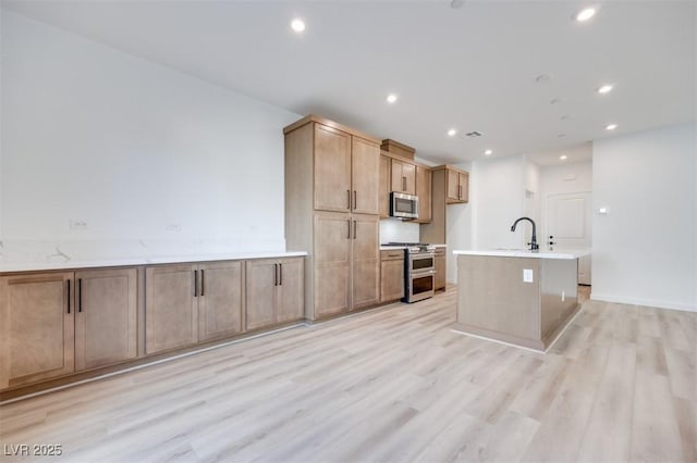 kitchen featuring appliances with stainless steel finishes, sink, light stone countertops, a center island with sink, and light hardwood / wood-style flooring