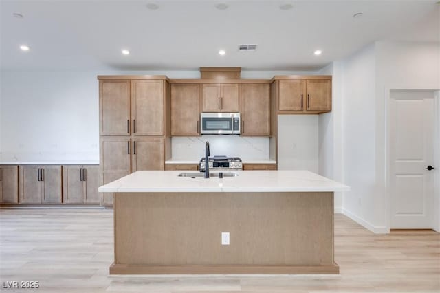 kitchen with an island with sink, light stone counters, and light wood-type flooring