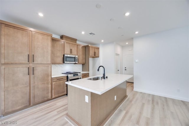 kitchen featuring stainless steel appliances, sink, light hardwood / wood-style floors, and an island with sink