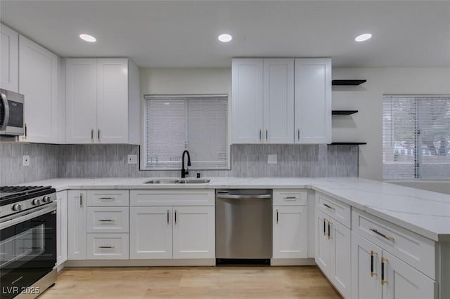 kitchen with appliances with stainless steel finishes, sink, white cabinets, and light hardwood / wood-style floors