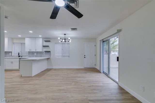 kitchen with decorative light fixtures, tasteful backsplash, white cabinetry, kitchen peninsula, and light wood-type flooring