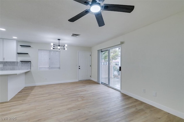 unfurnished living room featuring ceiling fan with notable chandelier and light wood-type flooring