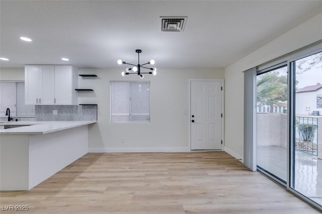 kitchen featuring tasteful backsplash, light wood-type flooring, a notable chandelier, pendant lighting, and white cabinets