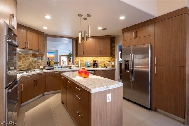 kitchen with light tile patterned floors, stainless steel appliances, a kitchen island, and brown cabinets