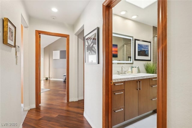 hall with recessed lighting, dark wood-style flooring, a sink, and baseboards