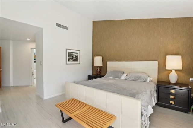 bedroom featuring an accent wall, wood finished floors, visible vents, and baseboards