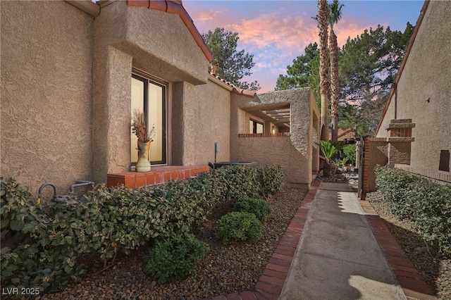 property exterior at dusk featuring a tile roof and stucco siding