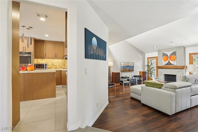 living room with a fireplace, wood finished floors, visible vents, baseboards, and vaulted ceiling