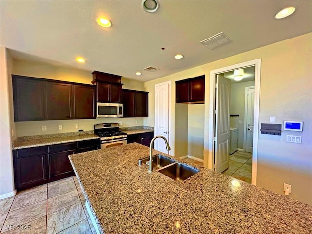 kitchen featuring stainless steel appliances, light stone countertops, sink, dark brown cabinets, and light tile patterned flooring