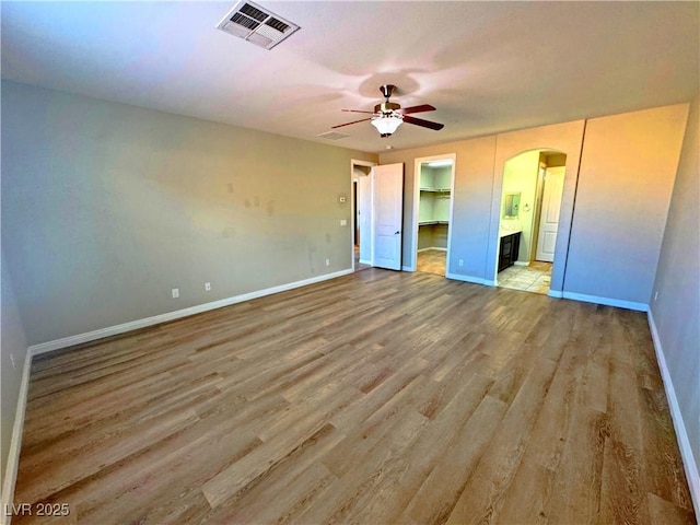 unfurnished bedroom featuring light hardwood / wood-style flooring, ensuite bath, a closet, a spacious closet, and ceiling fan