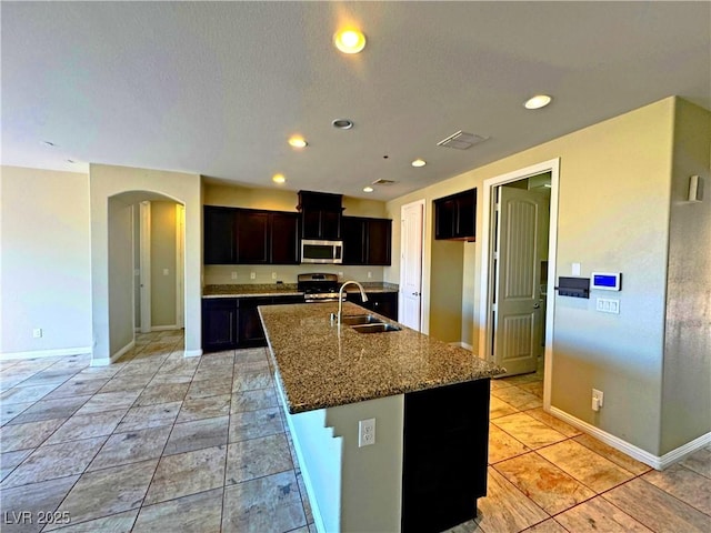 kitchen with a center island with sink, stainless steel appliances, stone counters, light tile patterned flooring, and sink