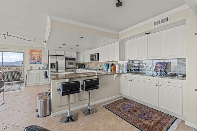 kitchen featuring light tile patterned floors, dark stone countertops, stainless steel appliances, white cabinets, and kitchen peninsula