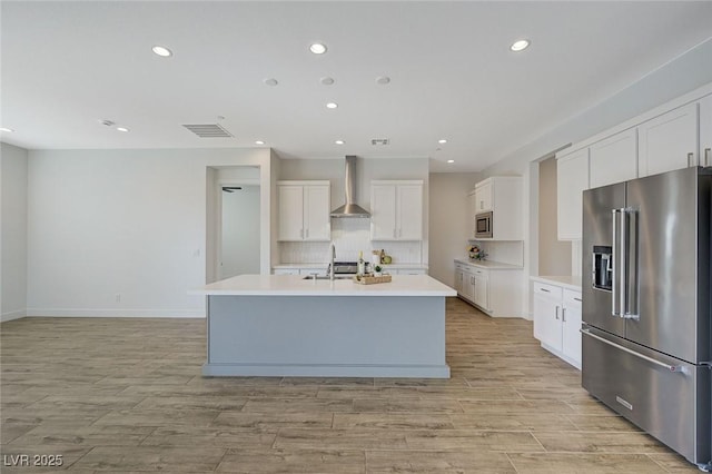 kitchen with sink, white cabinetry, stainless steel appliances, an island with sink, and wall chimney exhaust hood