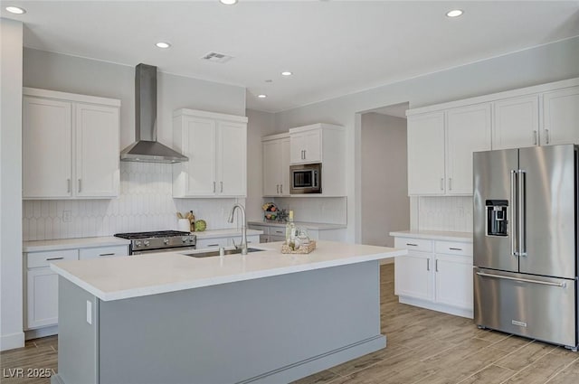 kitchen with high quality appliances, sink, white cabinets, and wall chimney exhaust hood