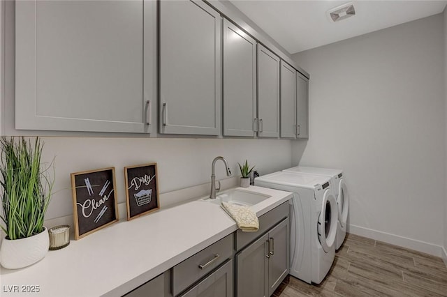 laundry room featuring sink, light hardwood / wood-style floors, cabinets, and washing machine and clothes dryer