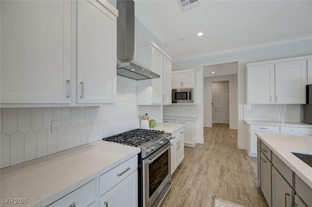 kitchen with stainless steel appliances, white cabinets, light stone counters, and wall chimney exhaust hood