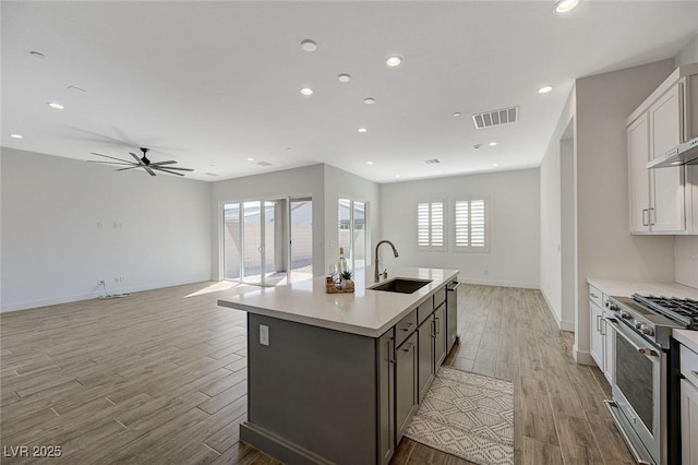 kitchen with sink, white cabinetry, stainless steel appliances, a center island with sink, and light wood-type flooring