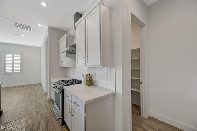 kitchen with white cabinetry, high end range, hardwood / wood-style floors, and backsplash