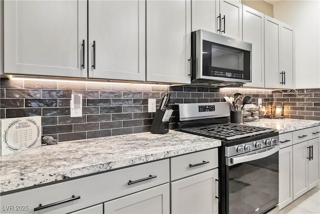 kitchen featuring light stone counters, backsplash, white cabinets, and appliances with stainless steel finishes