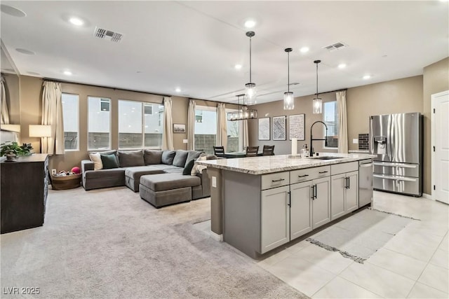 kitchen with hanging light fixtures, a center island with sink, appliances with stainless steel finishes, gray cabinets, and light stone countertops